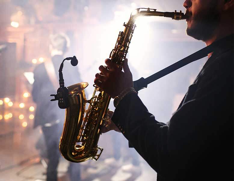 Profile view of classy saxophone player soloing over the corporate event band, seen in the background.