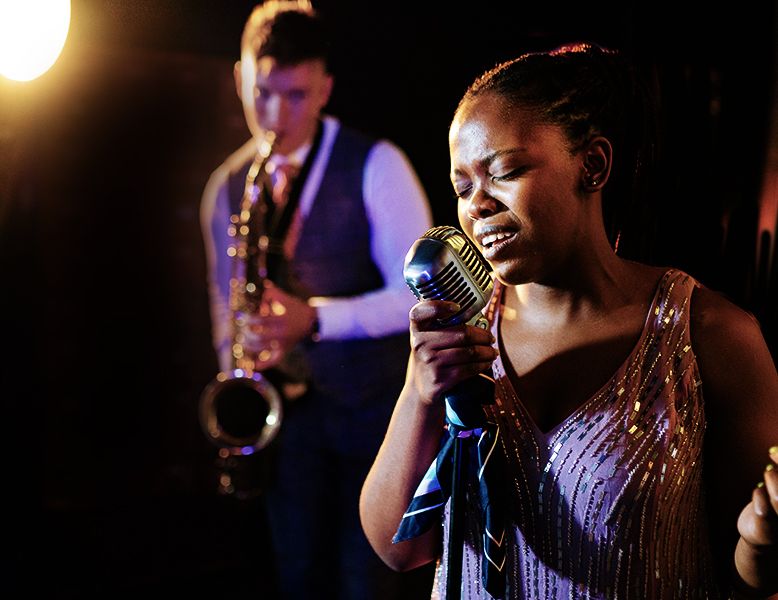 Young, attractive, black female vocalist at a mic accompanied by a bar mitzvah bands tenor sax player - both in classy formal dress - playing live music