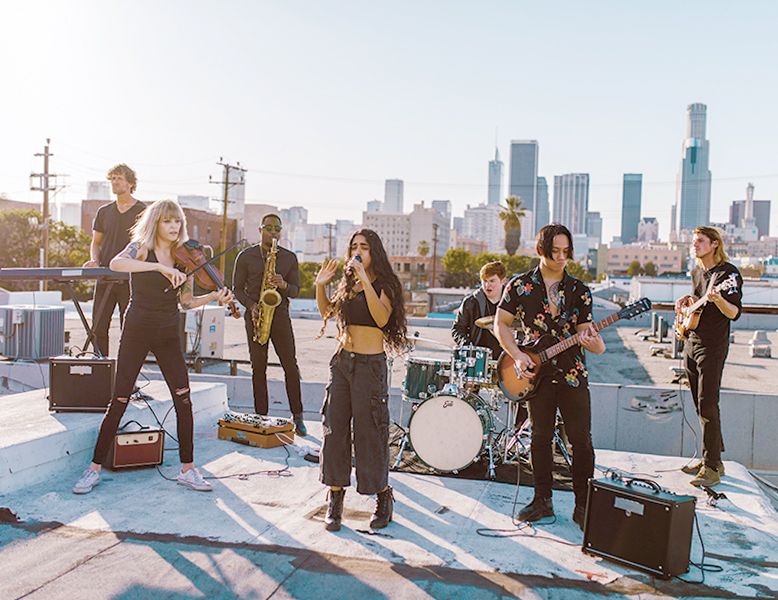 Live band with drums, guitar, bass, keyboard, young female singer, violin and saxophone playing a show at an NYC rooftop Bat Mitzvah celebration.